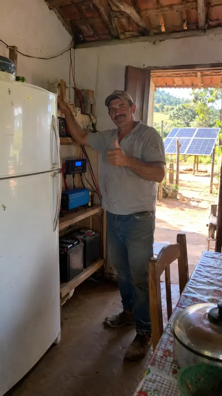João ao lado de geladeira e componentes de um sistema solar no sítio